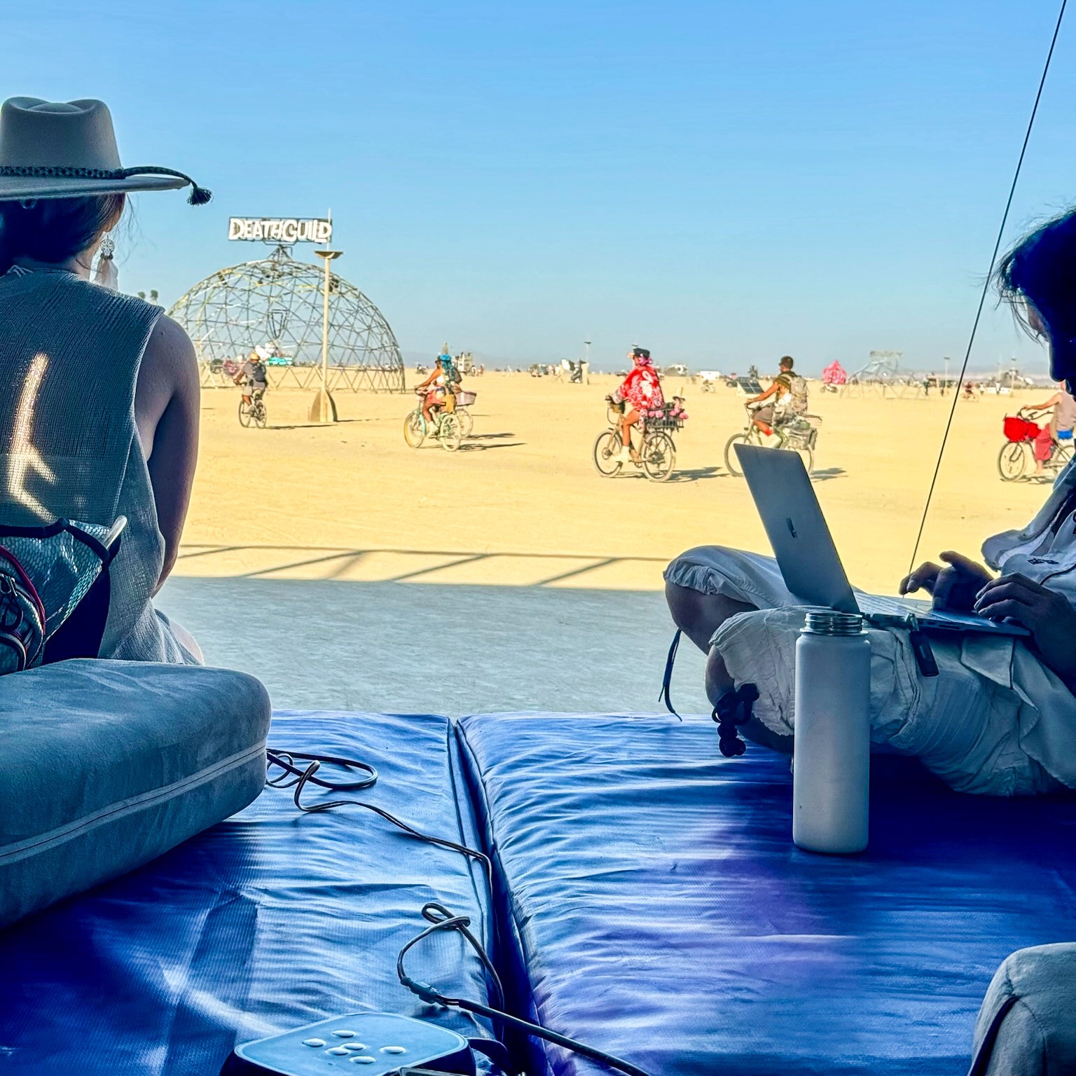 Members of the ResonantVibe crew relaxing on VAVE™ beds inside the Resonant Realm trailer overlooking the Playa at Burning Man 2024.